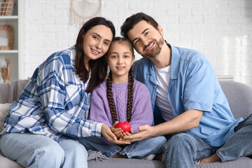 Happy couple with adopted girl and heart sitting on sofa at home