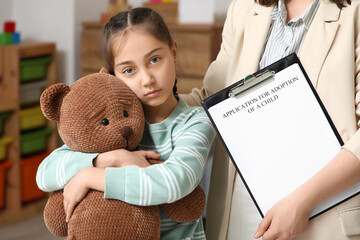 Sad girl with toy bear and social worker at orphanage