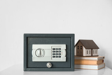 Modern safe with house model and books on shelf near light wall
