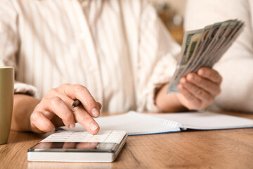 Fototapeta premium Senior woman with money calculating utility bills at table in kitchen, closeup