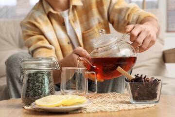 Young man pouring tea into glass cup at home, closeup