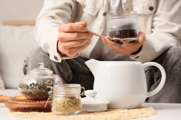 Young man pouring dry tea into teapot at home, closeup