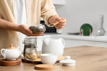 Young man pouring dry green tea into teapot in kitchen, closeup