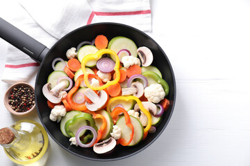 Frying pan with mix of vegetables, mushrooms and spices on white wooden table, top view. Space for text