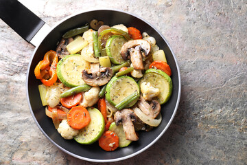 Different vegetables and mushrooms in frying pan on grey textured table, top view