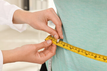Nutritionist measuring overweight woman's waist with tape in hospital, closeup
