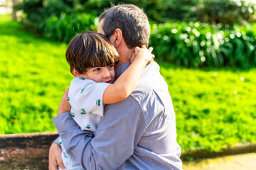 Fototapeta premium Grandfather embracing grandson in lush green park