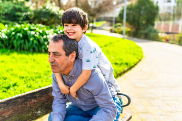 Grandfather carrying grandson piggyback in park