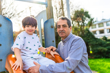 Grandfather helping grandson sliding down playground slide