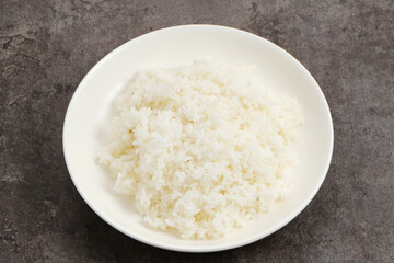 Cooked rice on white plate on dark background.
