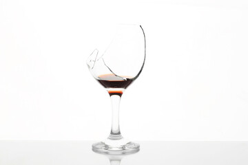 Broken glass with wine on table against white background