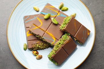 Pieces of Dubai chocolate bar with pistachios and knafeh on grey table, top view