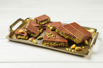 Pieces of Dubai chocolate bars with pistachios and knafeh on white wooden table