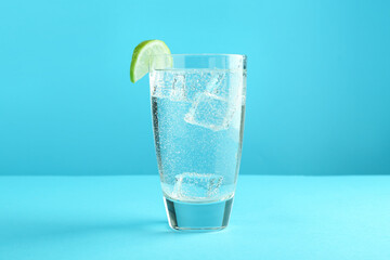 Soda water with lime and ice cubes in glass on light blue background