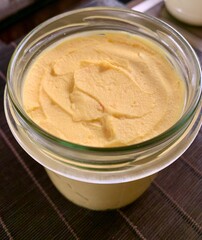 A glass jar filled with smooth, creamy hummus, featuring a bright yellow hue. It is freshly made, ideal for pairing with vegetables or pita bread