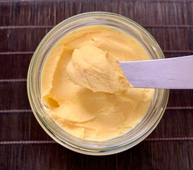 A glass jar filled with creamy yellow butter sits on a wooden surface, while a knife reveals its smooth and spreadable texture, inviting culinary use in various dishes