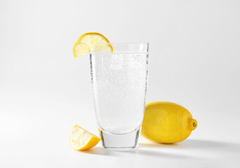 Refreshing soda water in glass and lemon on light grey background