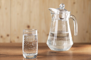 Refreshing soda water with ice cubes in glass and jug on wooden table