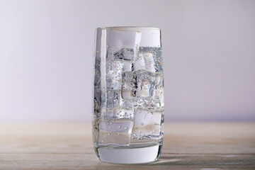 Refreshing soda water with ice cubes in glass on wooden table against light grey background, closeup