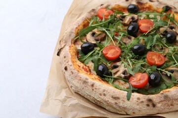 Tasty pizza with cherry tomatoes, black olives, mushrooms and arugula on white table, closeup. Space for text