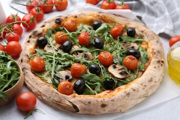 Tasty pizza with cherry tomatoes, black olives, mushrooms and arugula on white table, closeup