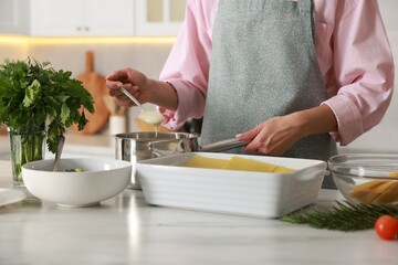 Woman making spinach lasagna at marble table indoors, closeup