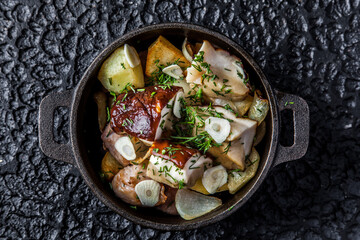 Soup in adrk black pot with garlik herb roasted potatos and fish.