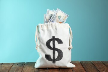 Dollar banknotes in burlap sack on wooden table against light blue background