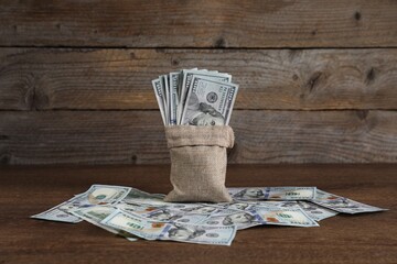 Burlap sack with dollar banknotes on wooden table