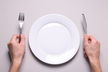 Man with cutlery and clean plate at light grey table, top view