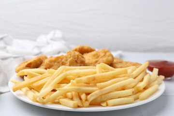 Tasty chicken nuggets and french fries with sauce on white tiled table, closeup. Space for text