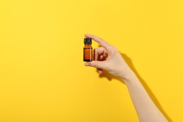 Woman with bottle of serum on yellow background, closeup. Body care product