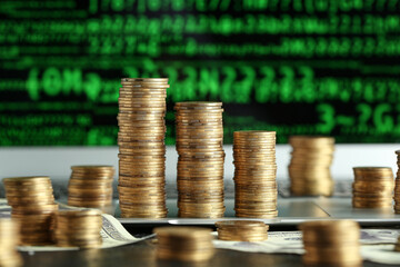 Stacks of coins on laptop with green programming code, closeup. Wealth concept