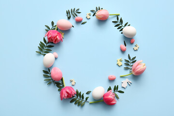 Frame made of Easter eggs, green leaves and flowers on blue background