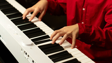 Fototapeta premium Close-up of hands playing a white digital piano, fingers pressing keys. Practice piano at home. Concept of education