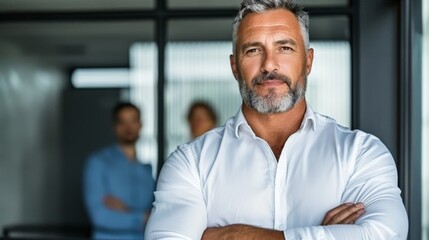 Confident mature caucasian male in white shirt at workplace with colleagues in background