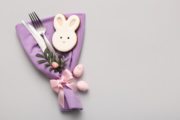 Stylish cutlery with sweet cookie, Easter eggs and leaves on grey background