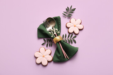 Stylish cutlery with sweet cookies, leaves and gypsophila flowers on lilac background. Easter...