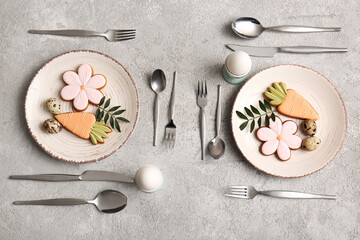 Beautiful table setting with sweet cookies, quail eggs and leaves on grey background. Easter celebration