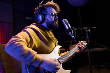 Man vocal artist singing in a recording studio with guitar. Male singer singing a song and playing...