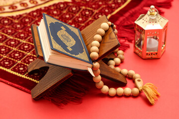 Rehal with Koran, prayer beads, rug and fanoos on red background. Ramadan celebration