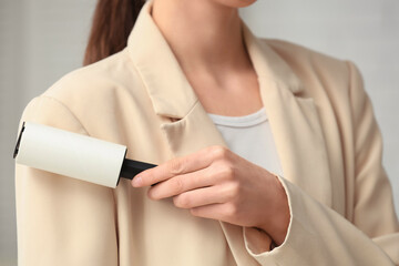 Woman cleaning her coat with lint roller at home, closeup