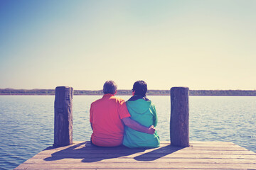 adult happy couple sitting together on a jetty by the lake and hugging each other