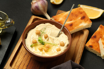 Bowl of delicious hummus with chickpeas, micro green and baked bread on black background