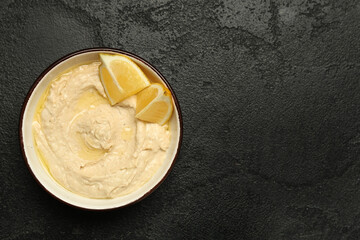 Bowl of delicious hummus with lemon on black grunge background
