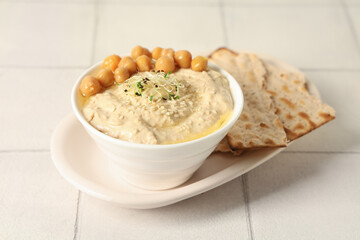 Bowl of delicious hummus with micro green, sesame seeds, chickpeas and crispbreads on white tile background
