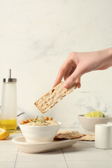 Woman eating delicious hummus with micro green, sesame seeds, chickpeas and crispbreads on white tile table