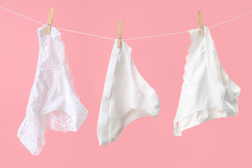 Female panties hanging on clothesline against pink background