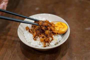 Chopsticks lifting braised pork above a bowl of braised pork rice.