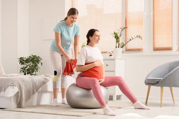 Obraz premium Young doula with scarf massaging pregnant woman on fitball in bedroom